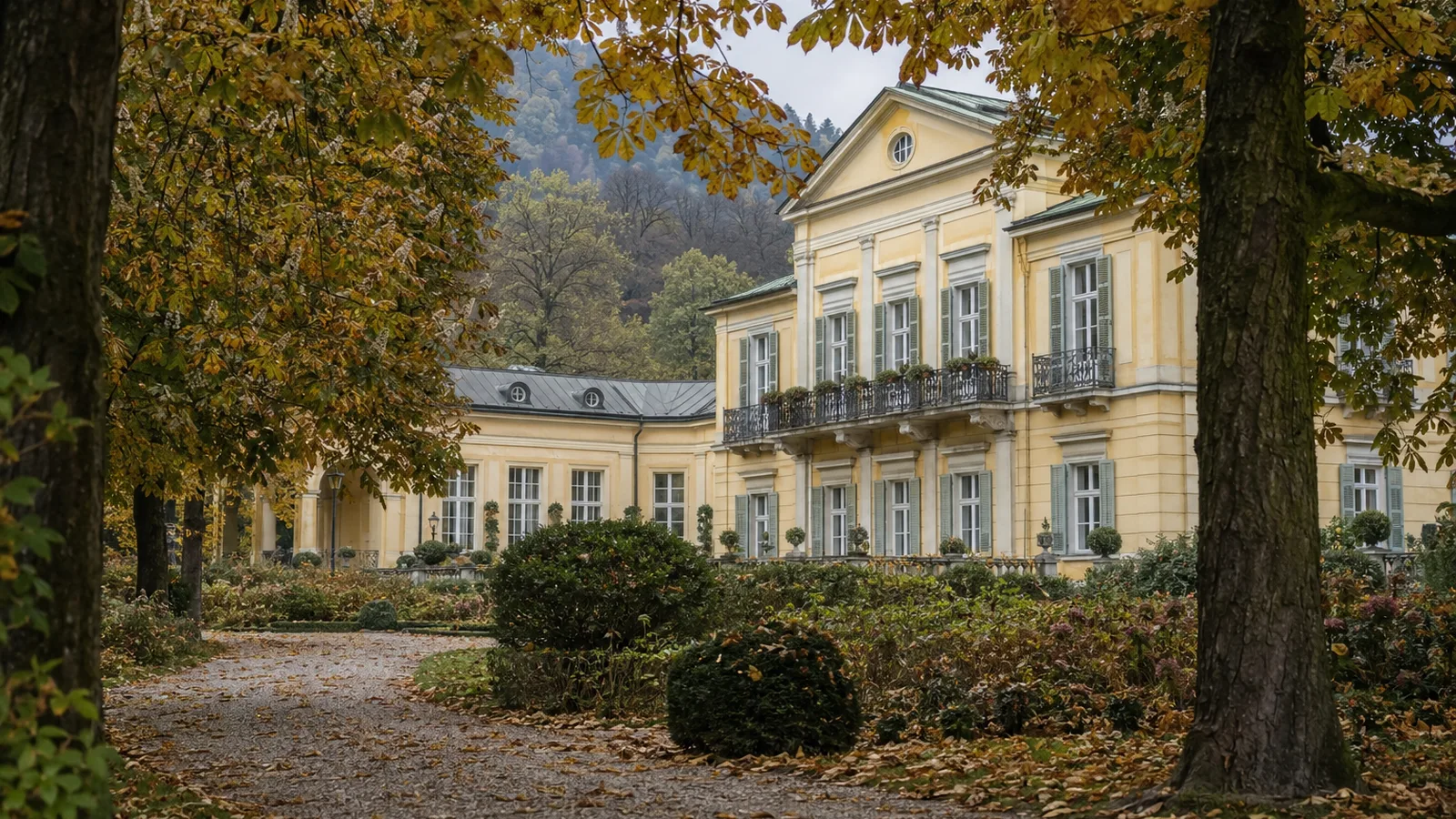 Das Hotel Kaiserkrone in Baden bei Wien, klassizistische Fassade, gesehen durch herbstlich gefärbte Kastanienbäume im Kurpark