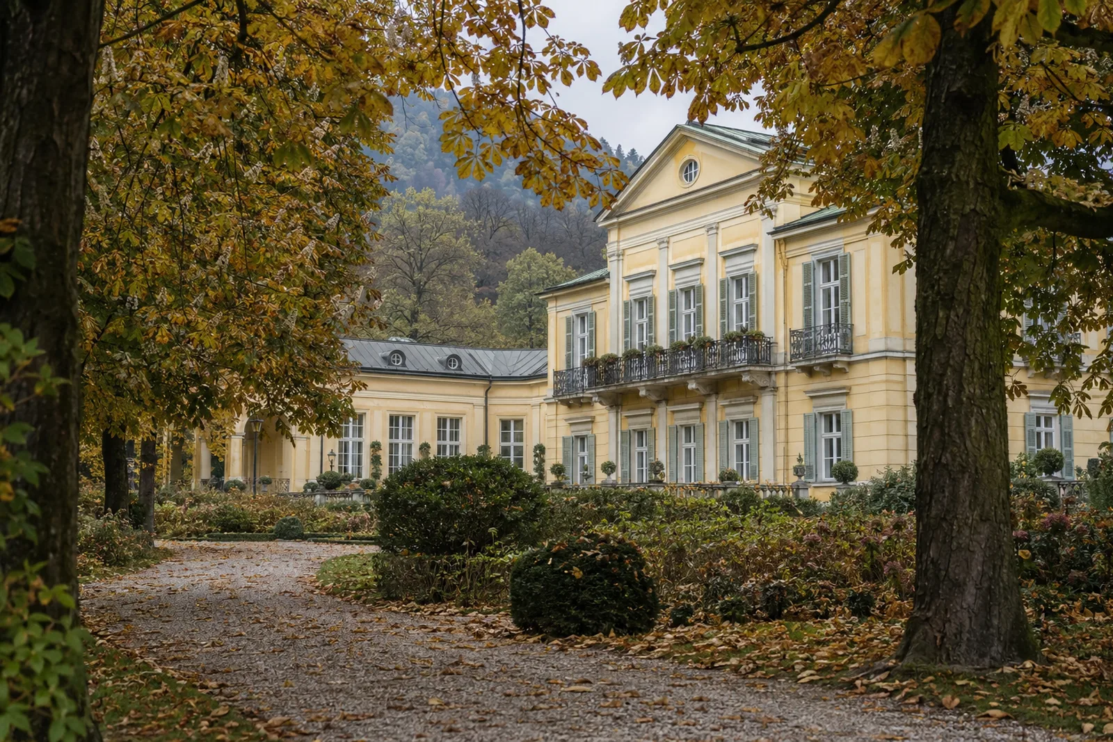 Das Hotel Kaiserkrone, ein klassizistisches Kurhotel in Baden bei Wien, gesehen durch herbstlich gefärbte Kastanienbäume im Kurpark